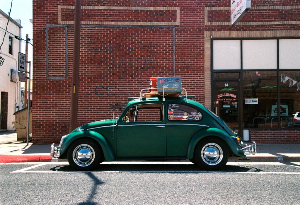 A vibrant daytime street scene featuring a vintage green Volkswagen Beetle parked in front of a red brick building in a small American town. Nikon F5 Kodak Portra 400.