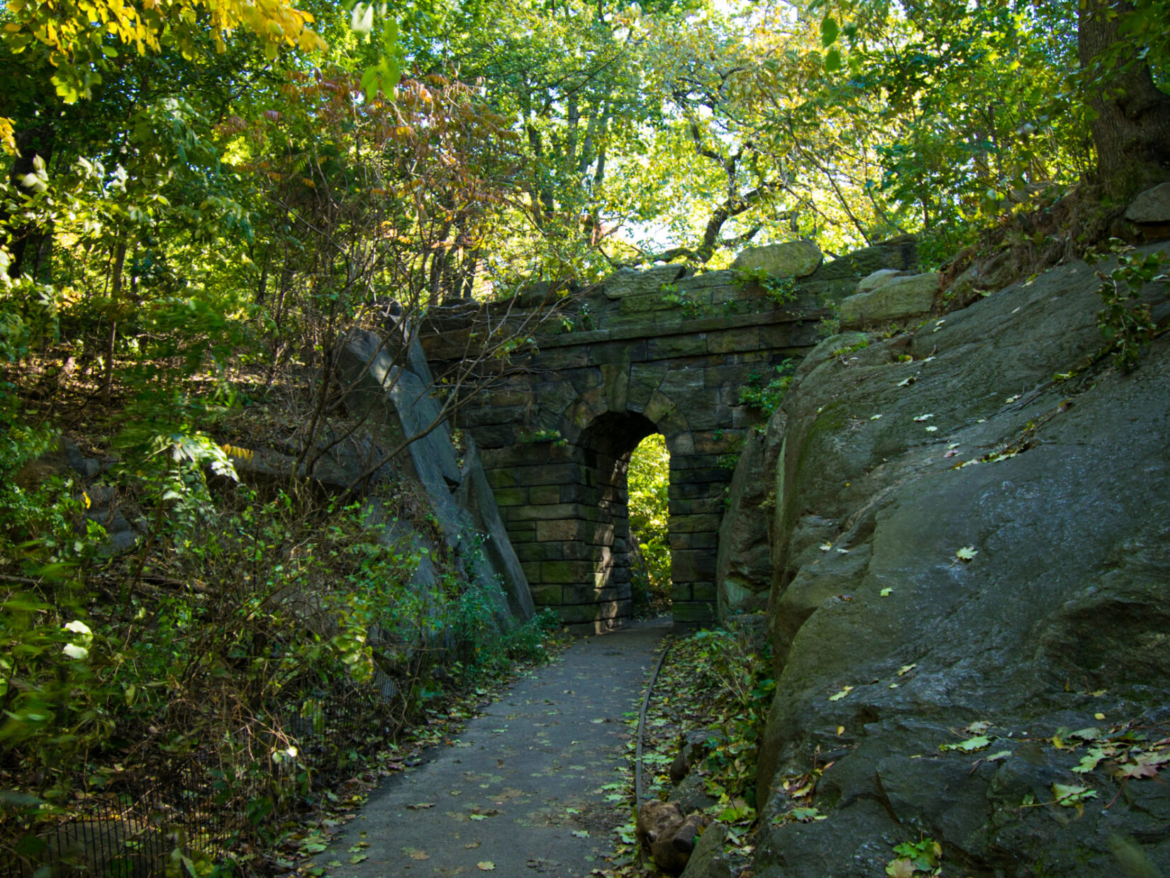 A curved path leads to a stone arch, partly obscured by trees.