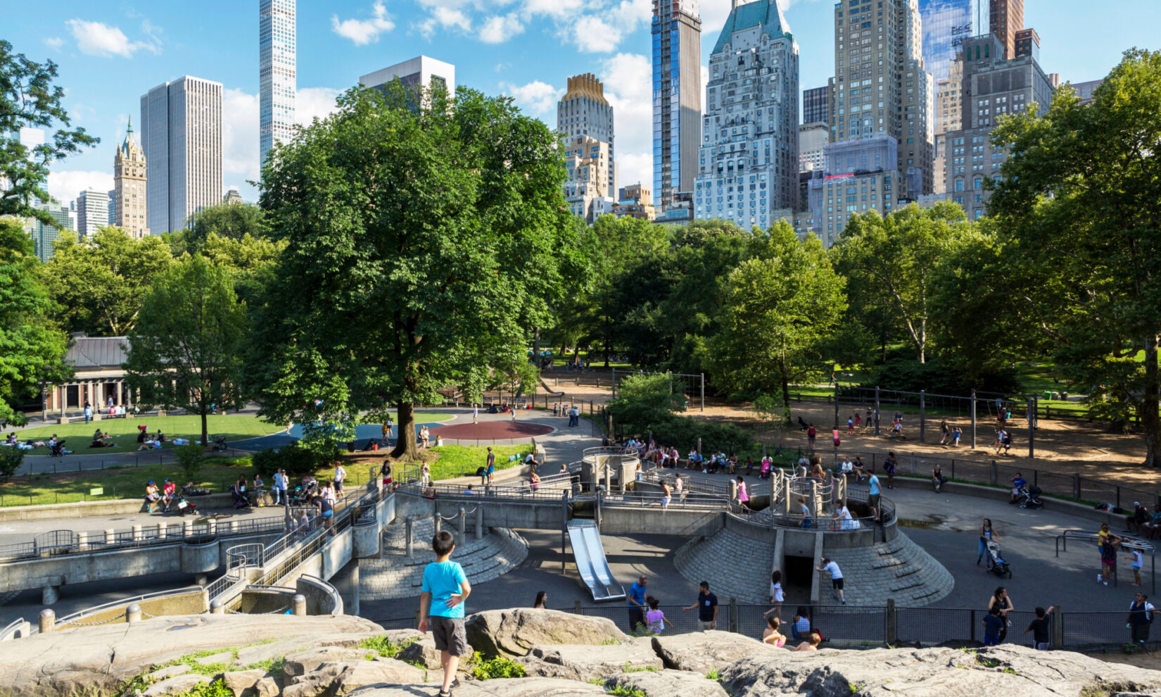 Children playing in the Heckscher Playground, with tall buildings in the background