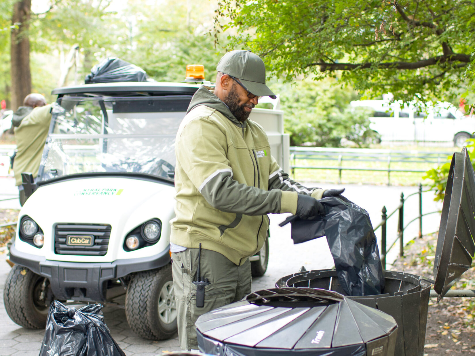 A Conservancy staff member, dressed in the organization's green uniform and hat, puts a new garbage bag in one of Central Park's receptacles.