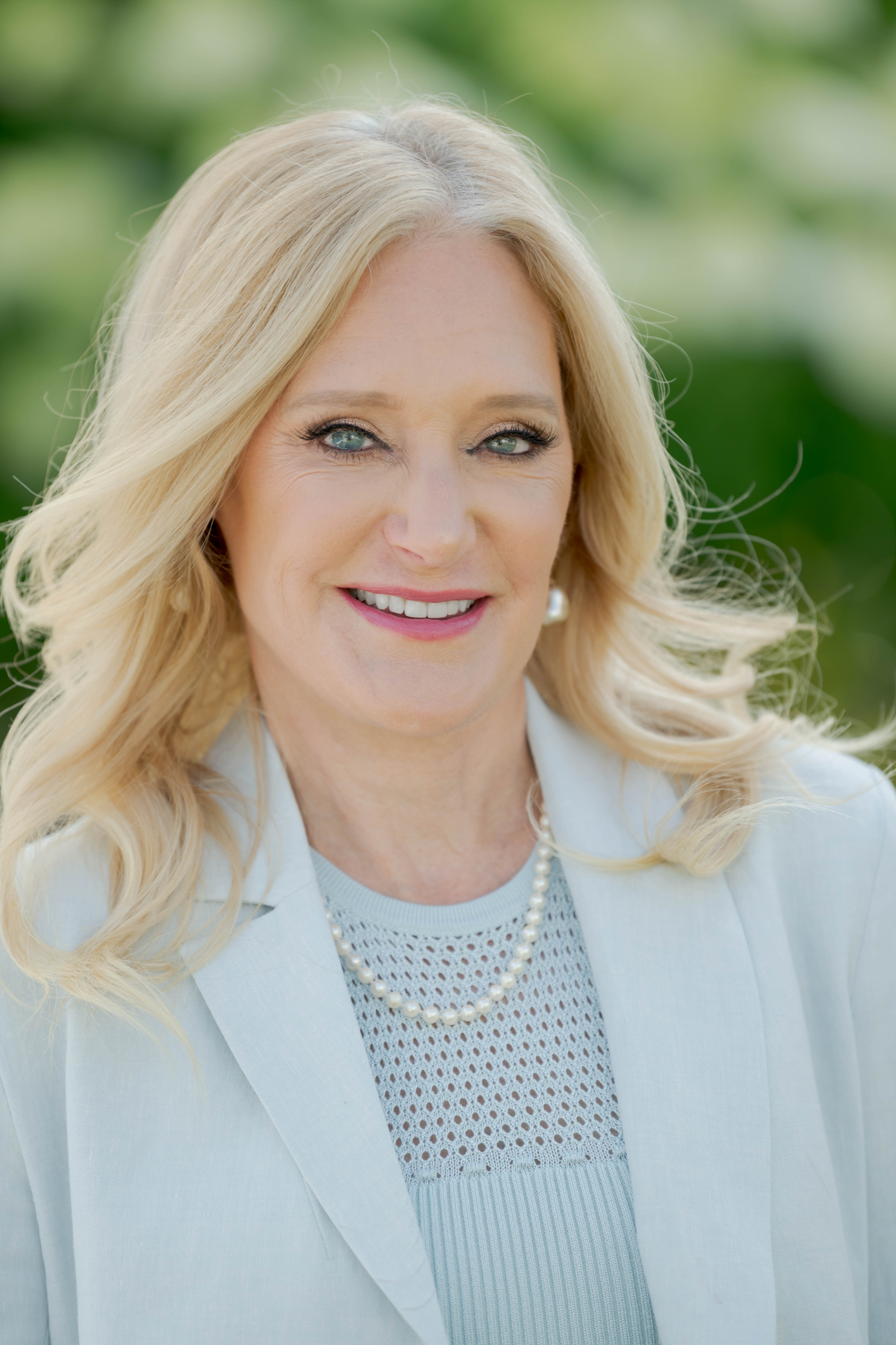 Betsy Smith, President & CEO of Central Park Conservancy, smiling and standing with arms crossed outdoors in Central Park, wearing a blue jacket.