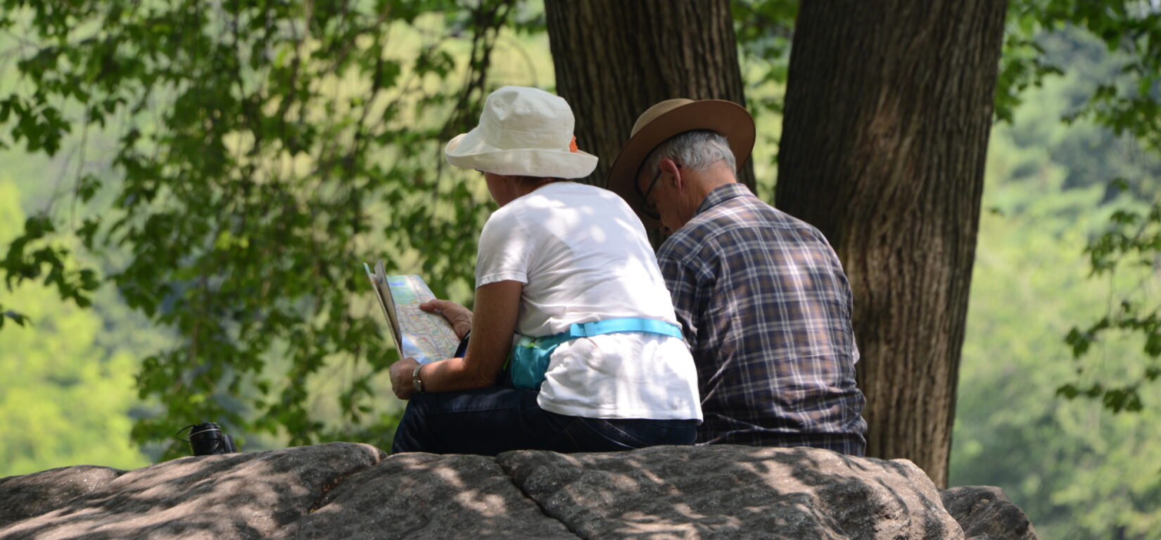 Two people sitting on a rock facing away from us, in Central Park, NYC